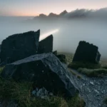 Raw Obsidian by Yuano: Giant volcanic fragments on a misty mountain plateau illuminated by a sharp beam of light.