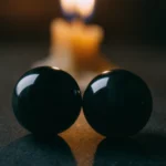 Sacred Light by Yuano: Two obsidian spheres reflecting candlelight in a dramatic chiaroscuro setting.