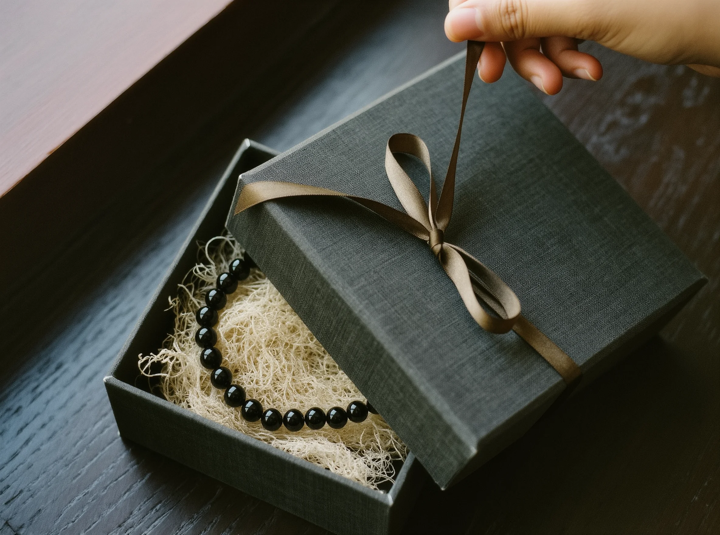 The Gift of Grace: Why We Exchange Sacred Tokens 1 Sacred Token by Yuano: A handcrafted obsidian necklace in a luxury charcoal gift box with a silk ribbon.