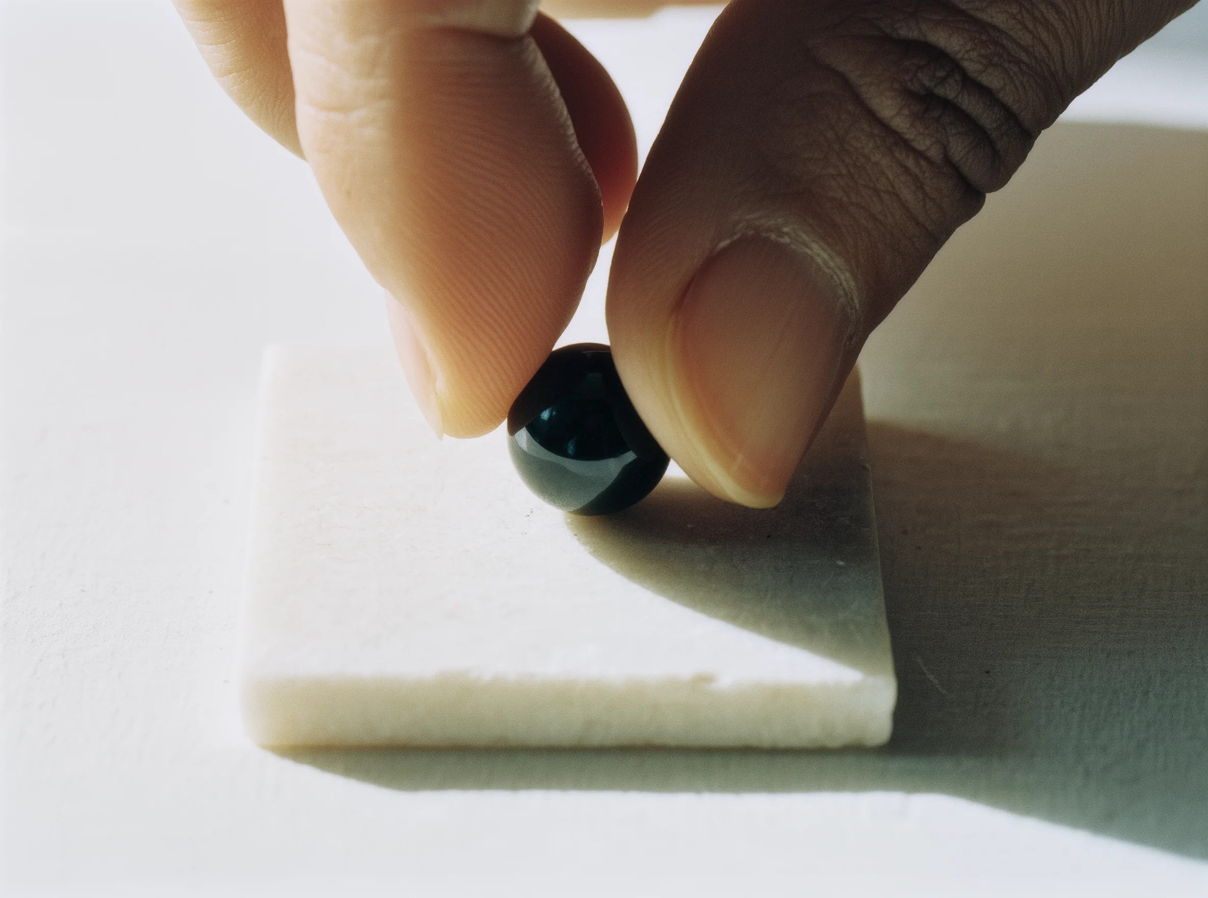 The First Stone: Marking the New Beginning in Grace 1 The First Stone by Yuano: A sacred obsidian bead being placed on a white stone base by an artisan's hand.
