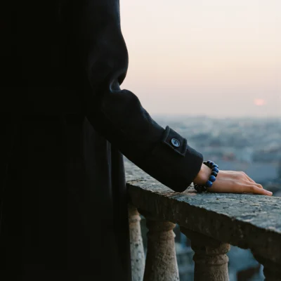 Covenant No. 05 — Lifestyle Observational Poise Covenant No. 05: Astral Path bracelet worn on a wrist against a black coat on a stone balcony at sunset.