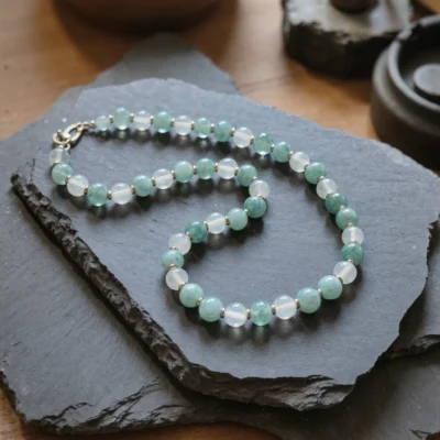Fluidity No. 01 — The Rising Tide Main Perspective Fluidity No. 01: The Rising Tide hand-knotted necklace featuring Xinjiang Aquamarine and Sichuan Moonstone on dark slate.
