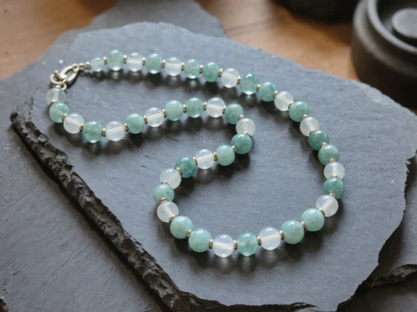 Fluidity No. 01 — The Rising Tide Main Perspective Fluidity No. 01: The Rising Tide hand-knotted necklace featuring Xinjiang Aquamarine and Sichuan Moonstone on dark slate.