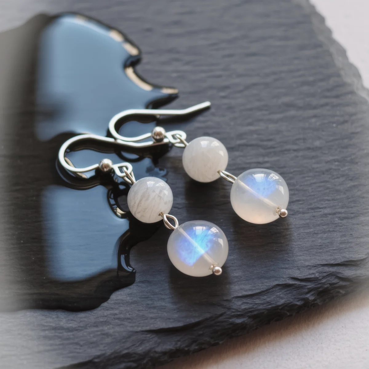 Fluidity No. 03 — Moon on Water Main Perspective Fluidity No. 03: Moon on Water hand-knotted earrings featuring Sichuan Moonstone and Anhui White Agate on a wet dark slate.
