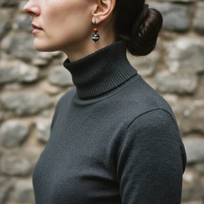 Fortress No. 10 — Lifestyle Observational Poise Fortress No. 10: Ancient Shield earrings worn by a model in a dark grey turtleneck against an ancient stone wall.
