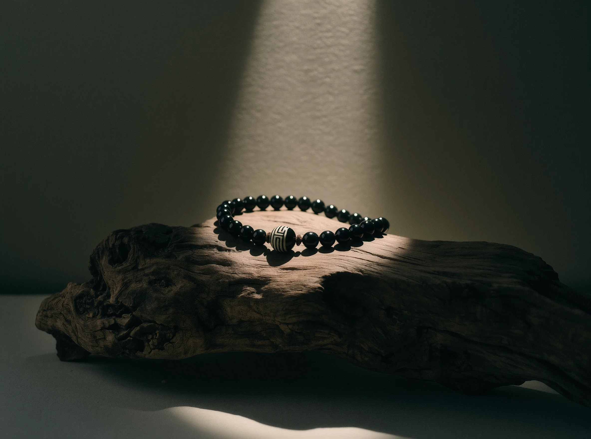 Home 1 Monastic Luxury Jewelry by Yuano: A handcrafted obsidian necklace with an etched focal stone resting on weathered driftwood under a dramatic spotlight.