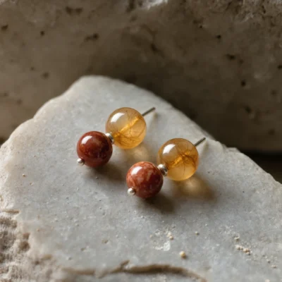 Origin No. 10 — Terrestrial Glow Main Perspective Origin No. 10: Terrestrial Glow hand-knotted earrings featuring Xinjiang Jinsiyu and Sichuan Nanhong on a natural stone altar.