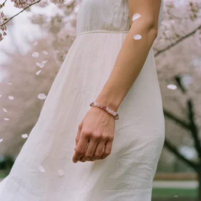 Serenity No. 06 — Lifestyle Observational Grace Serenity No. 06: Petal Dance bracelet worn by a model in a white dress under falling cherry blossoms.