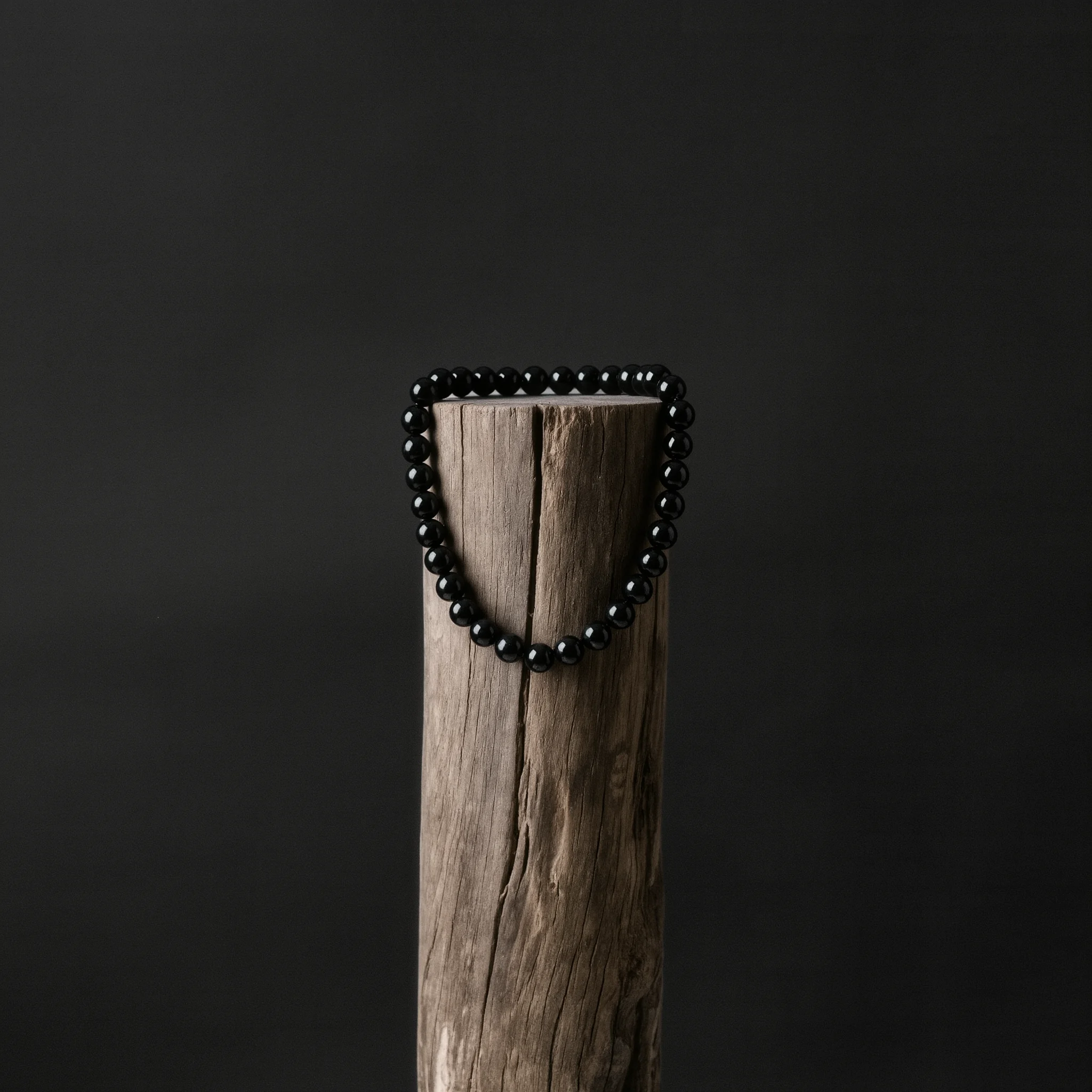 Home 4 Sovereign Stillness Jewelry by Yuano: A handcrafted obsidian relic necklace draped over a weathered wooden pillar in a dramatic monastic setting.