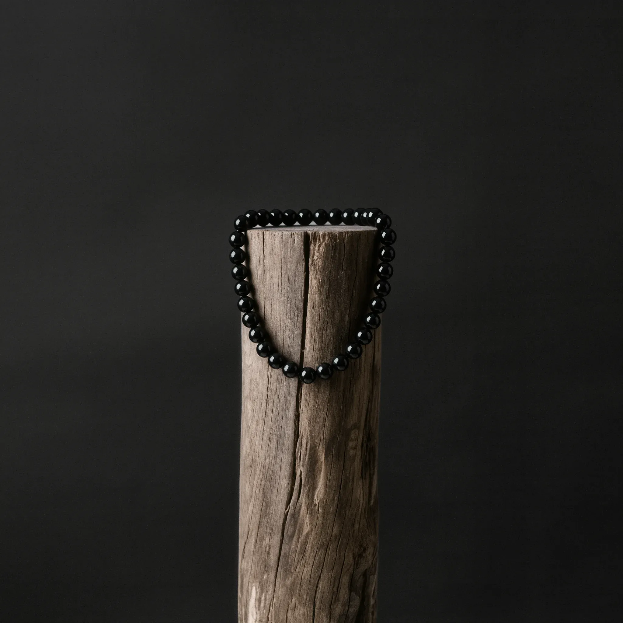 Home 4 FAQ for Sovereign Stillness Jewelry: Handcrafted obsidian relic bracelet on an aged wood pillar against a minimalist dark background.